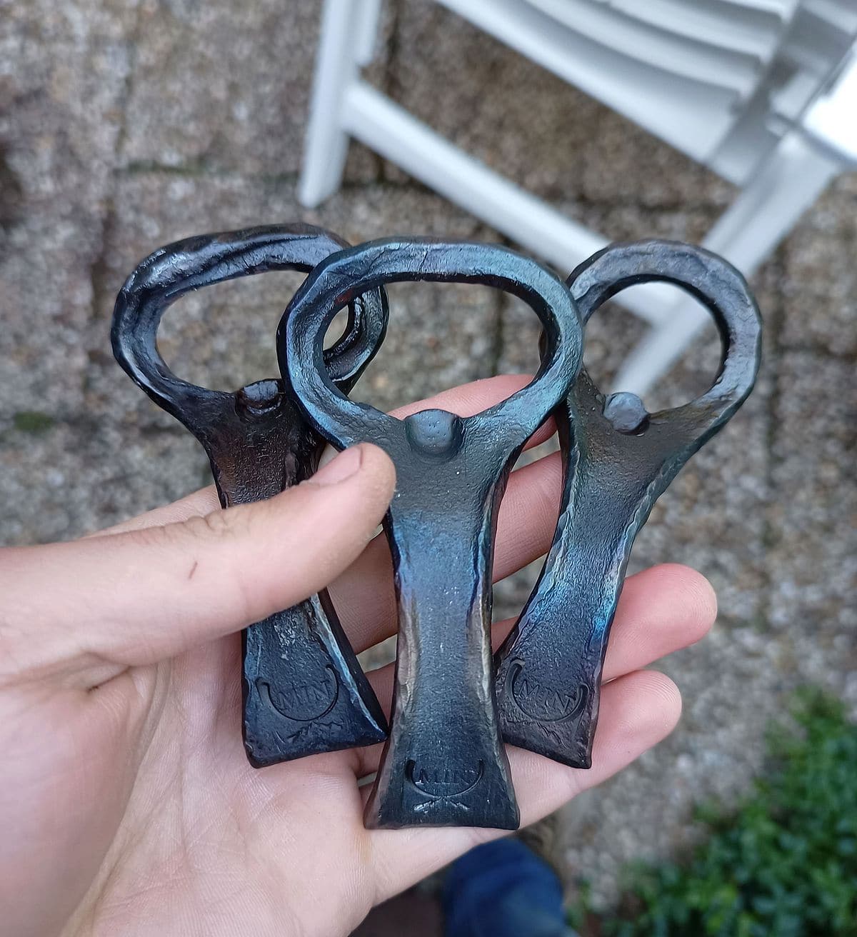 Drie handgesmede flesopeners met blauwe aanloopkleuren en het smidsmerk MIN