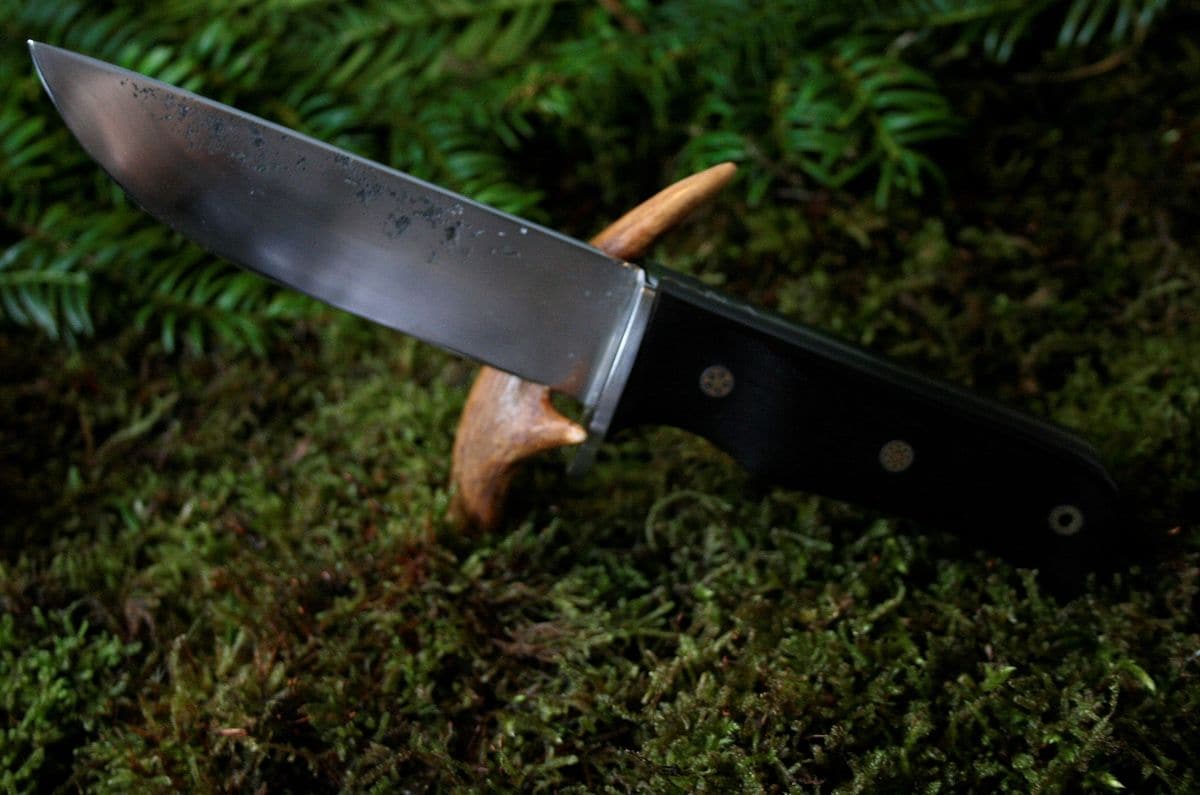 Handgesmeed outdoormes met zwart heft en mozaïekpinnen, op mos