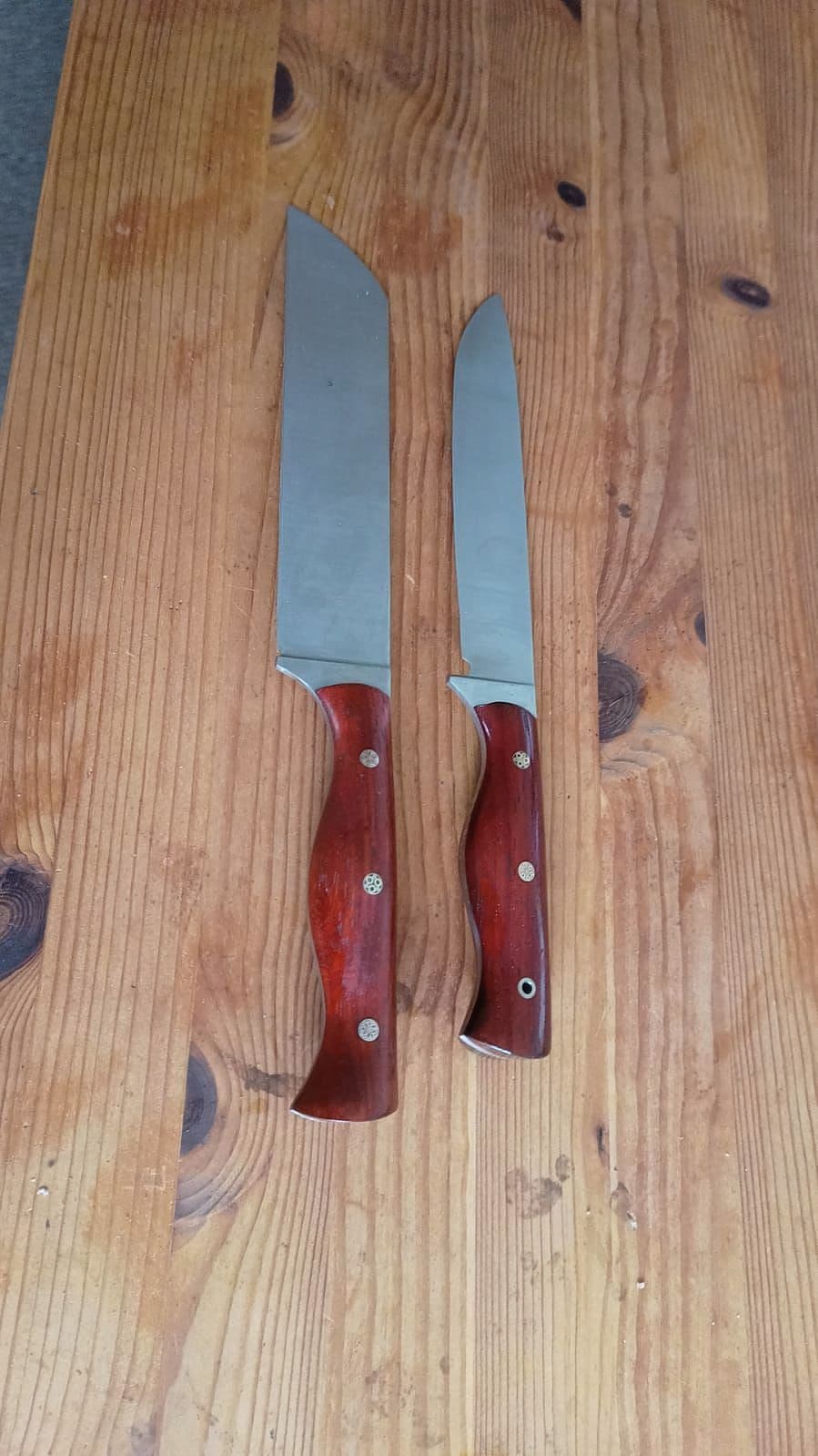 Twee handgemaakte keukenmessen met rood houten heft op een houten tafel