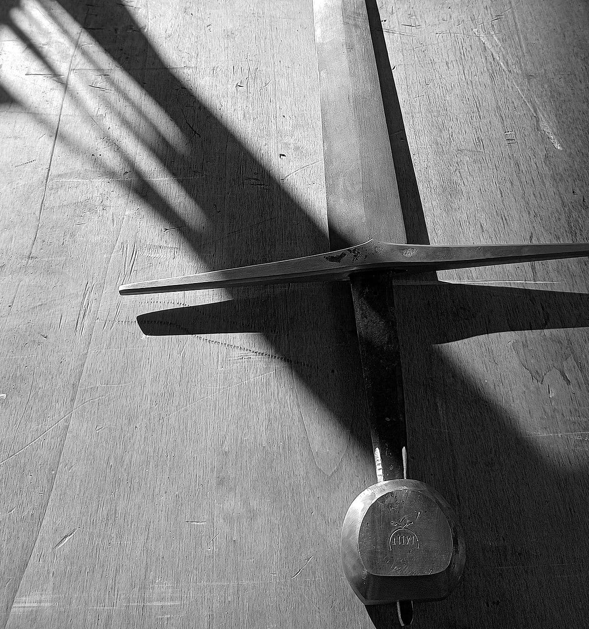 Gevest van een handgesmeed langzwaard met pareerstang en pommel, in strijklicht