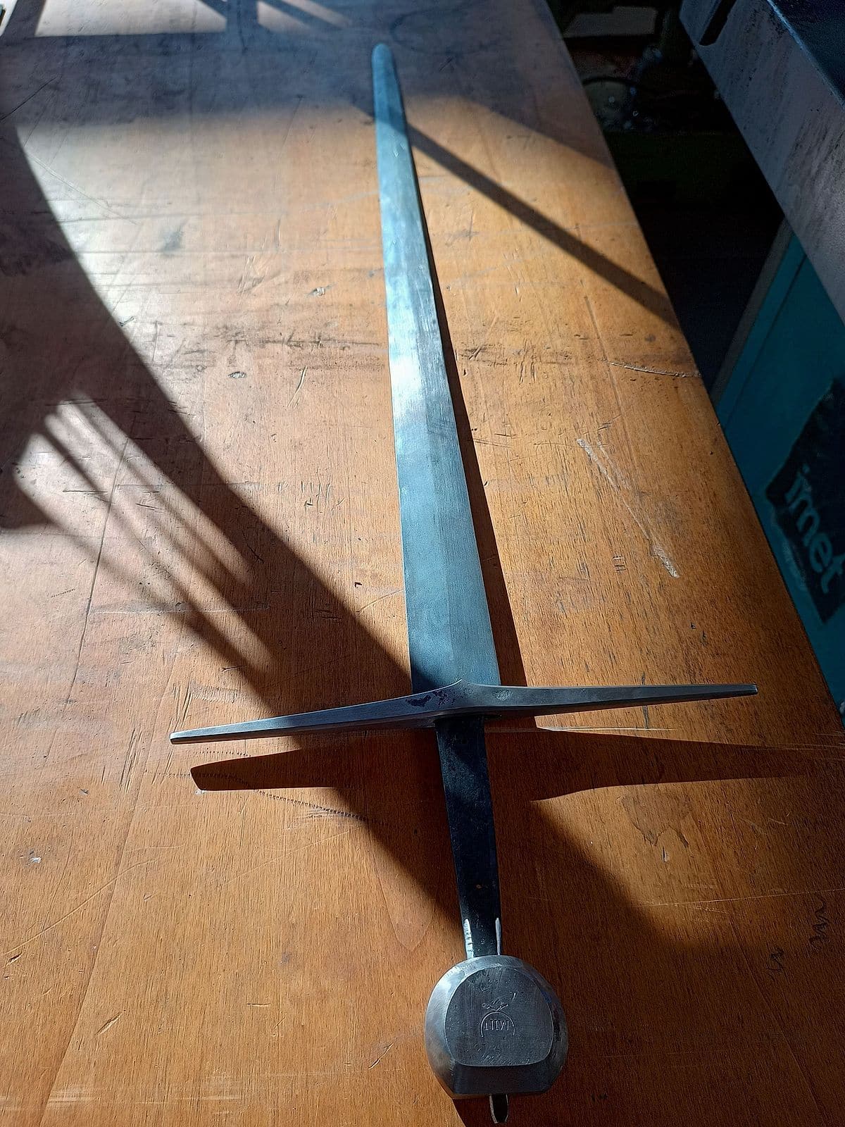 Zwaard met blauw aangelopen kling op een houten werkbank in strijklicht