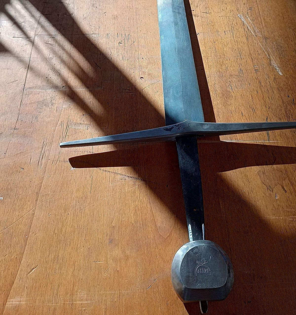 Gevest van het handgesmede langzwaard met pareerstang en pommel met smidsmerk, in strijklicht
